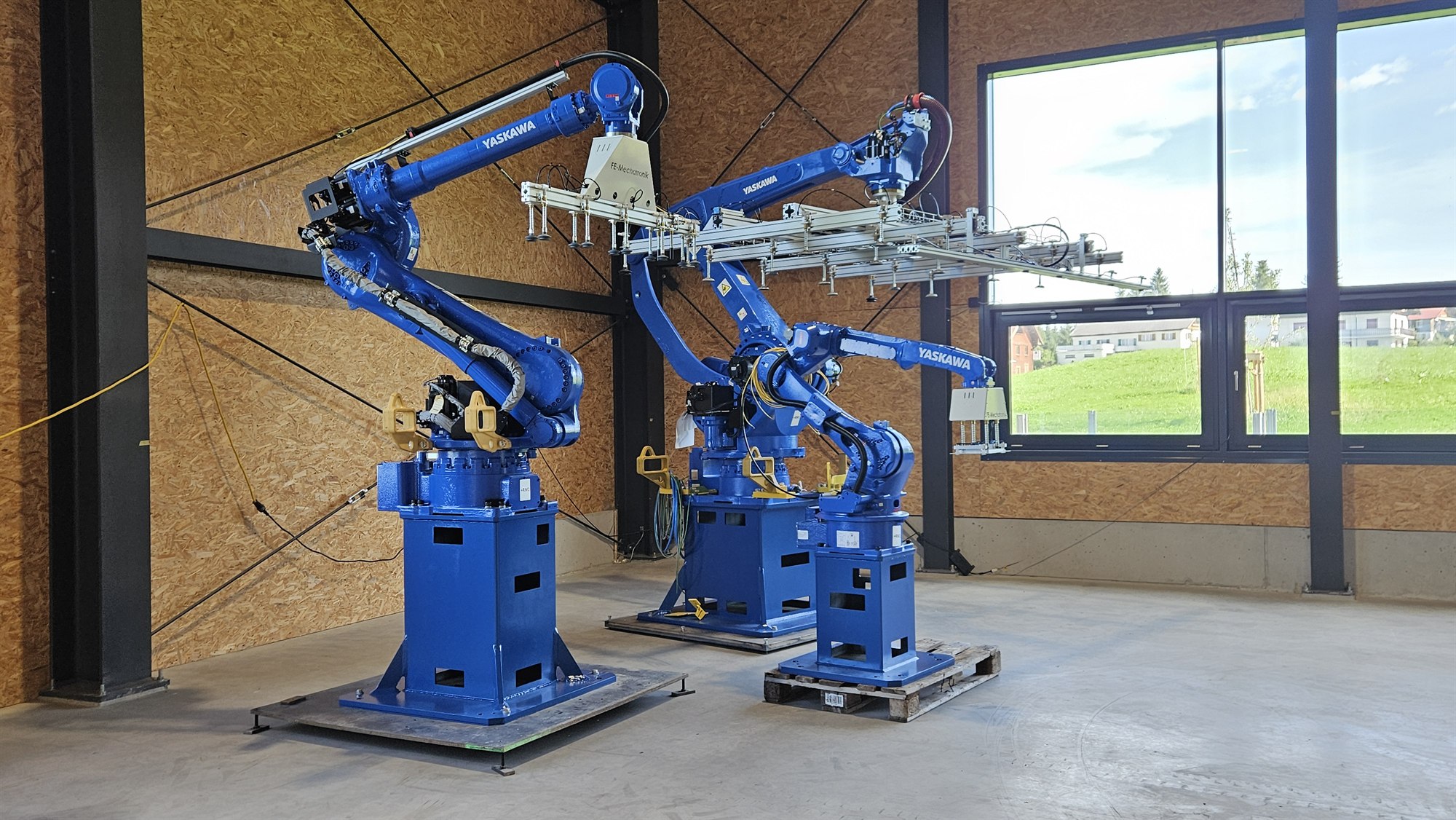 Drei Yaskawa-Industrieroboter mit großflächigen Greifersystemen in der Werkshalle